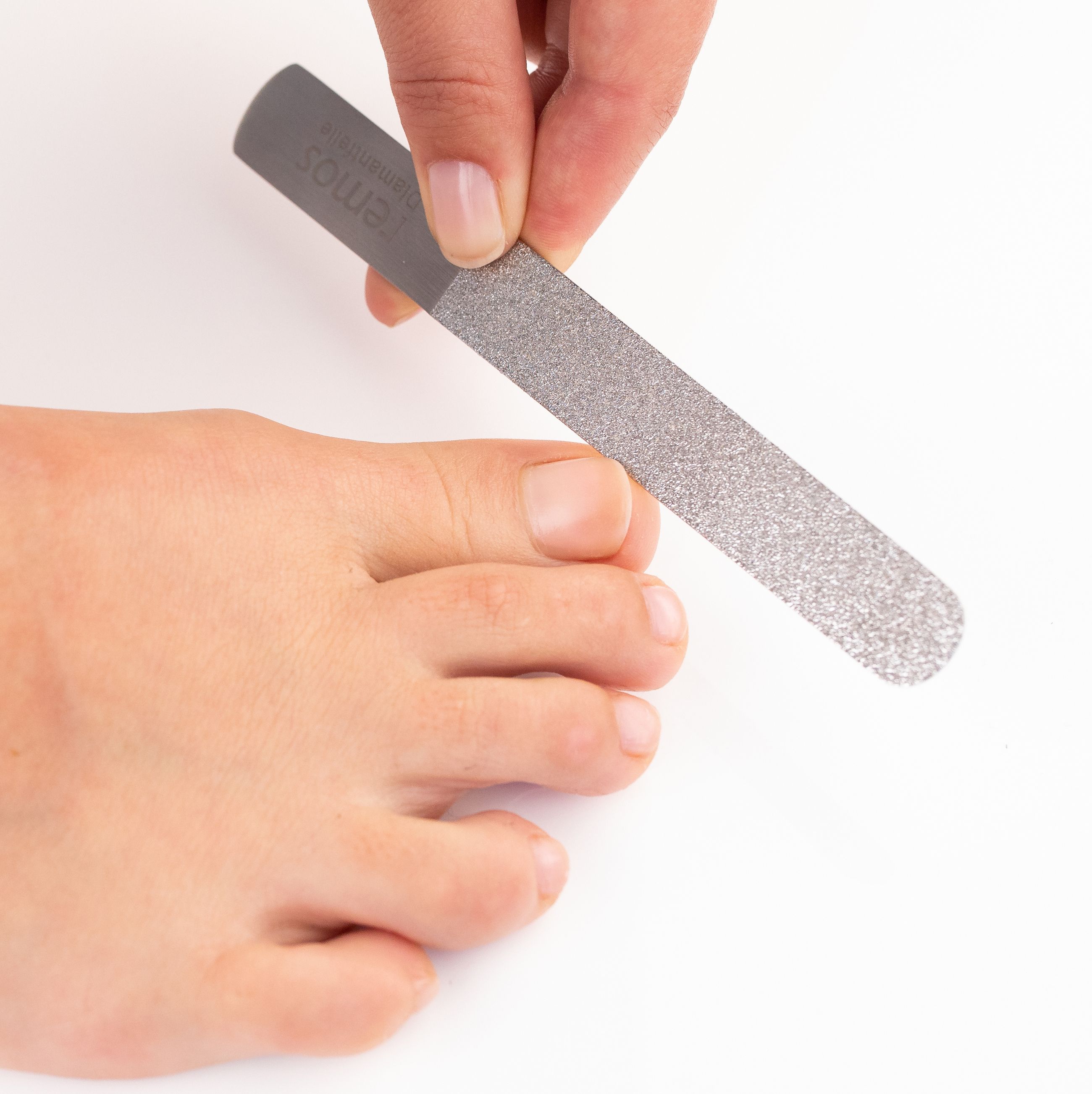 Eine Hand benutzt eine Diamantnagelfeile, um einen Zehennagel zu feilen.