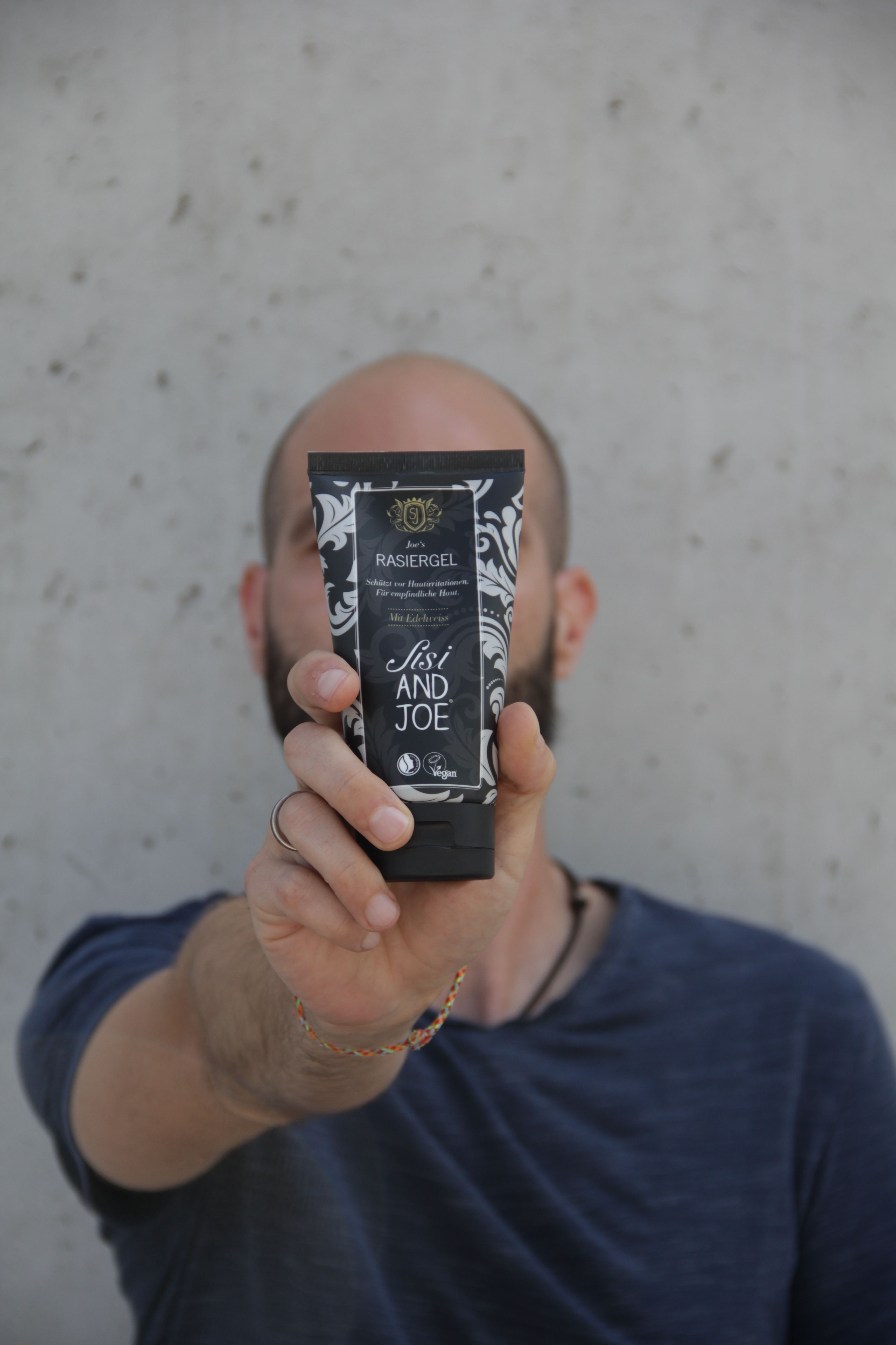 Person hält eine Tube Rasiergel vor sich. Schwarze Tube mit weißem Muster und Text: Sisi and Joe Rasiergel.