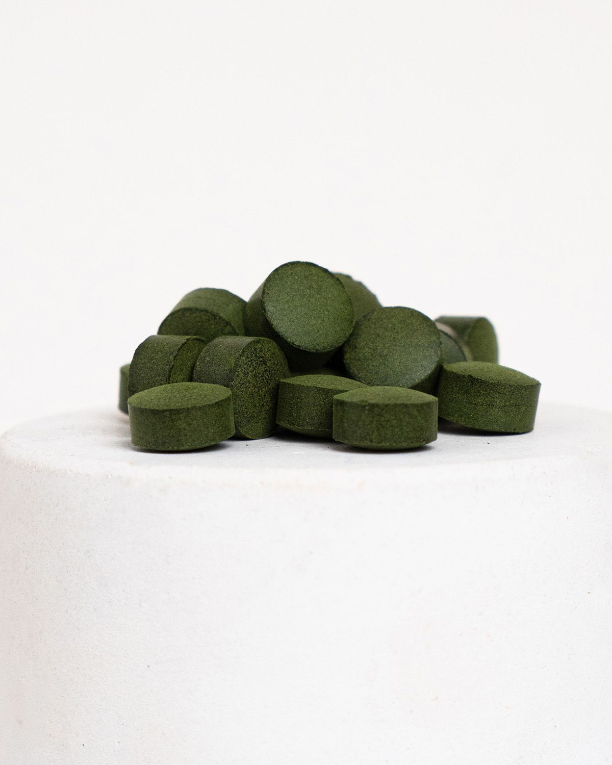 Haufen grüner Tabletten auf weißem Untergrund. Runde Form, flache Oberseite, dunkelgrüne Farbe.