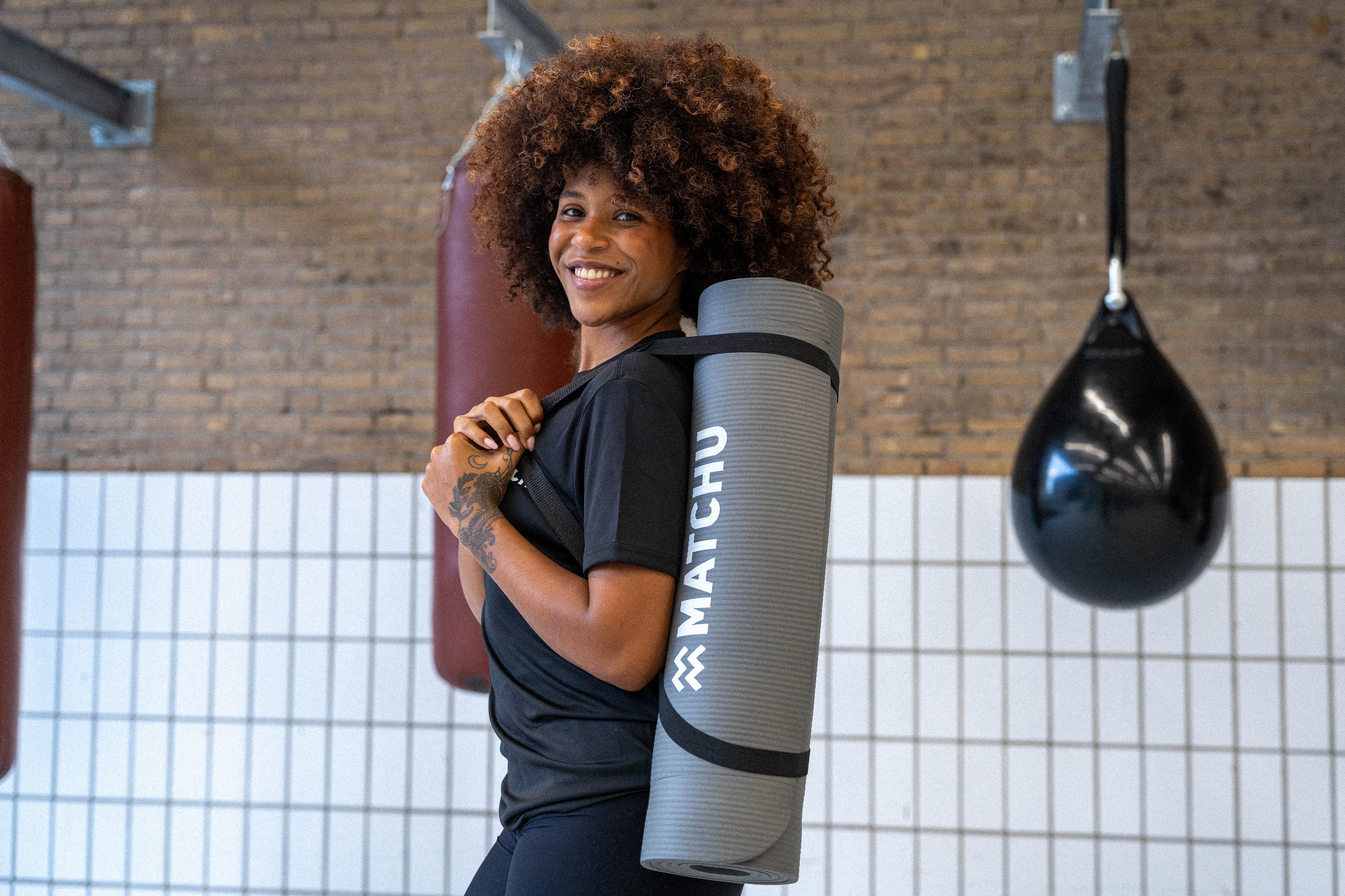 Frau mit Fitnessmatte über der Schulter. Auf der Matte steht "MATCHU".