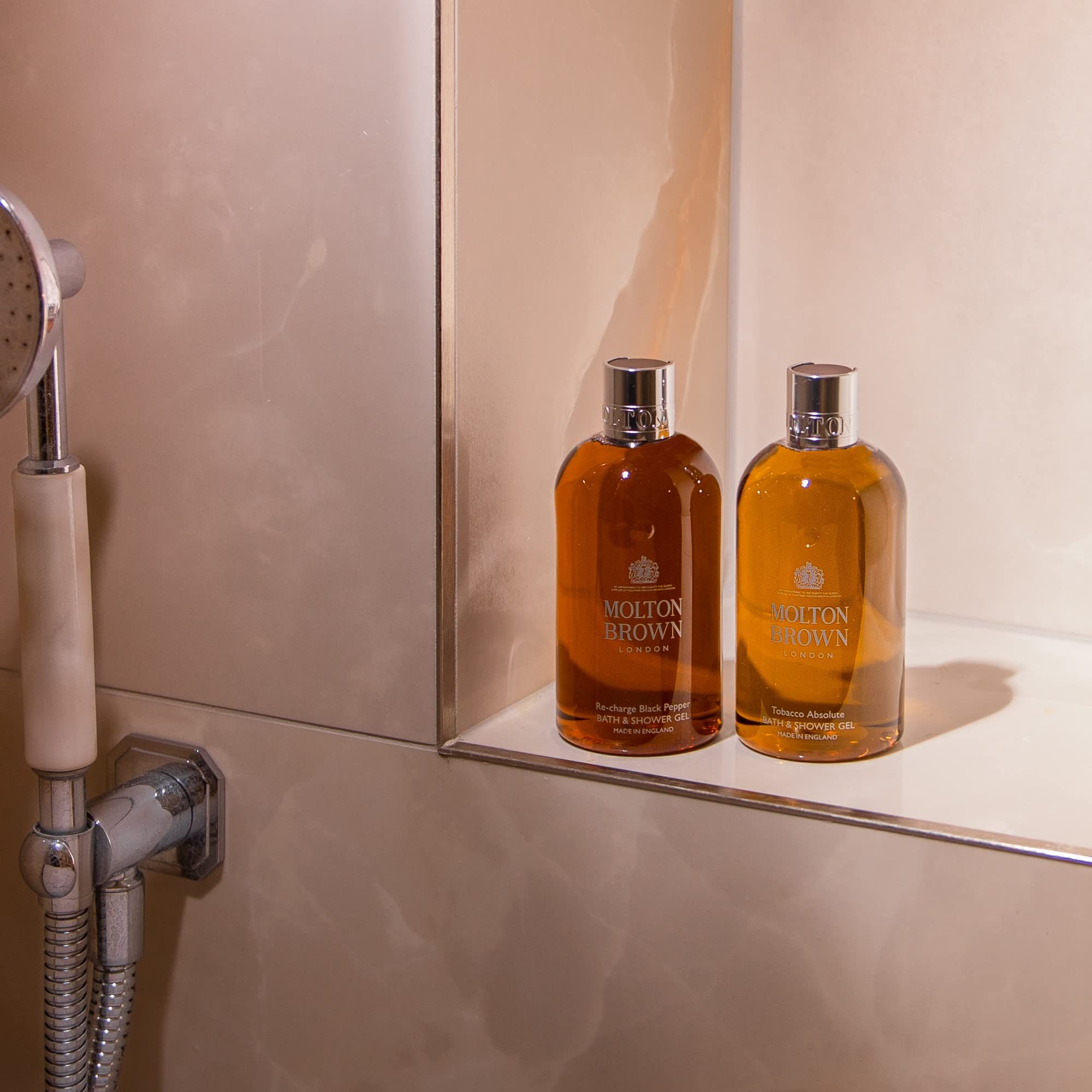 Zwei Flaschen Molton Brown Duschgel in einer Dusche. Silberne Duscharmatur links.