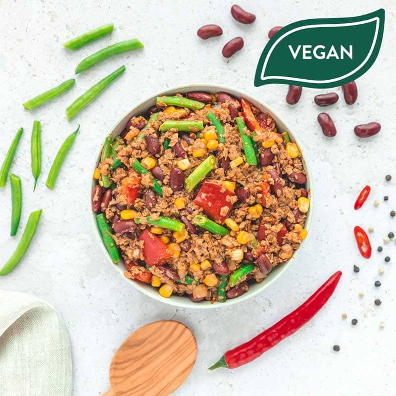 Veganes Gericht mit Bohnen, Gemüse und Chili. Draufsicht. Auf hellem Untergrund. Vegan-Siegel. Rote Chili.