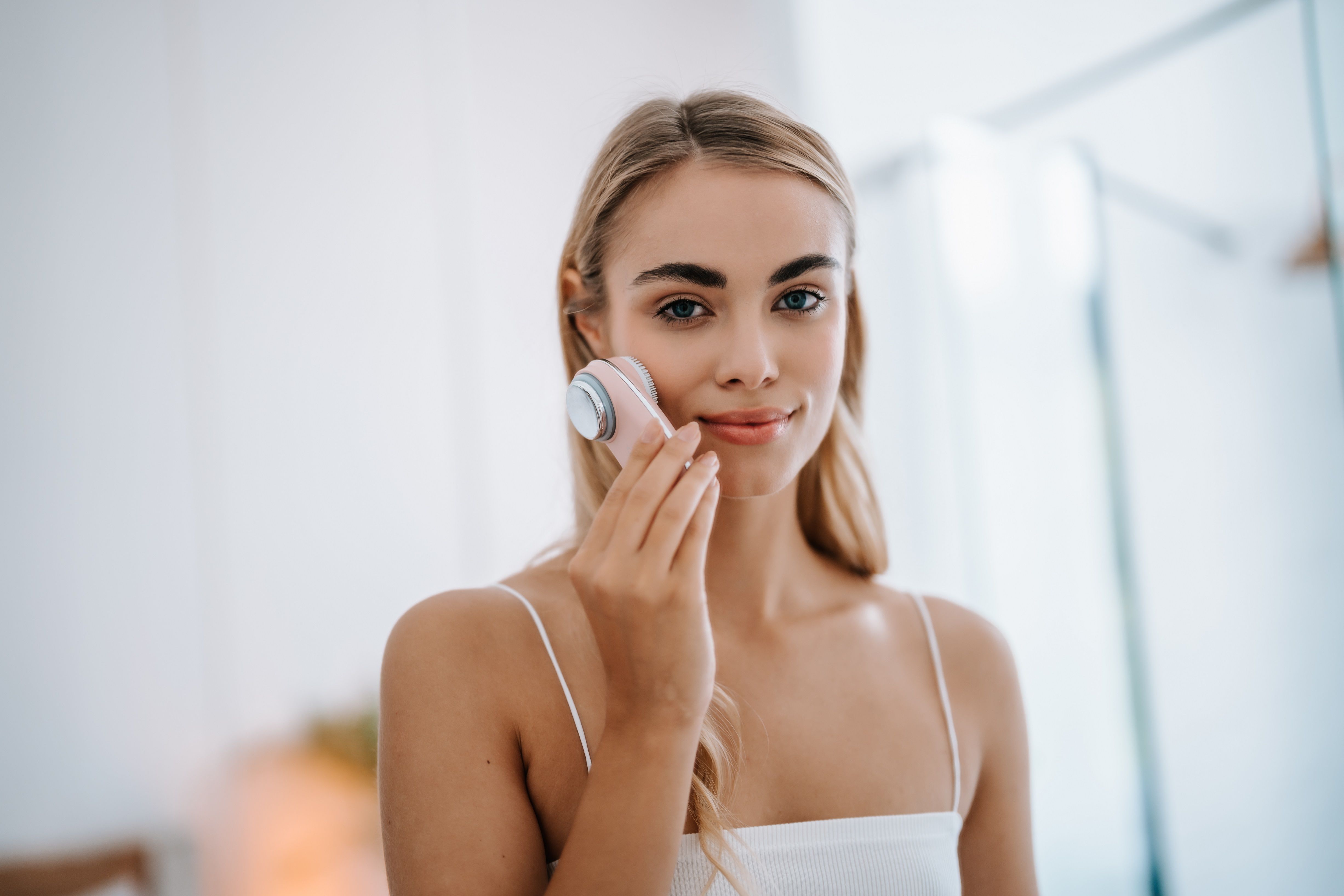 Eine Frau hält ein rosa Gerät an ihrer Wange. Das Gerät hat eine runde Form. Die Frau lächelt in die Kamera.