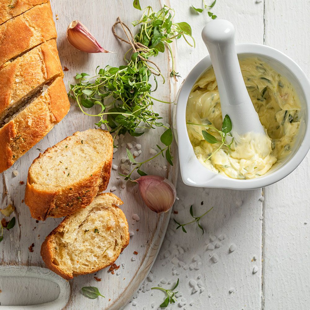 Baguette, Knoblauchzehen, Kräuter und Kräuterbutter in Schüssel. Auf Holzbrett. Kräuterbutter mit Zitronenthymian.
