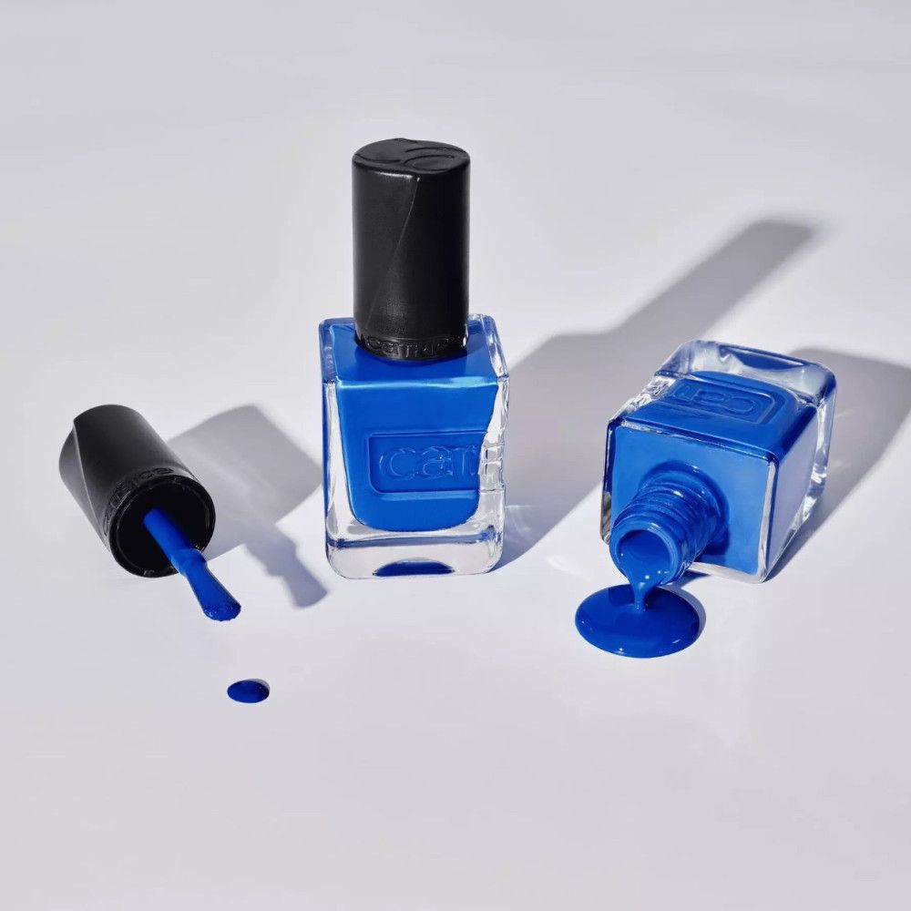 Drei blaue Nagellackflaschen, eine mit Deckel, eine umgekippt mit Lack, eine aufrecht. Der Markenname Catrice ist sichtbar.