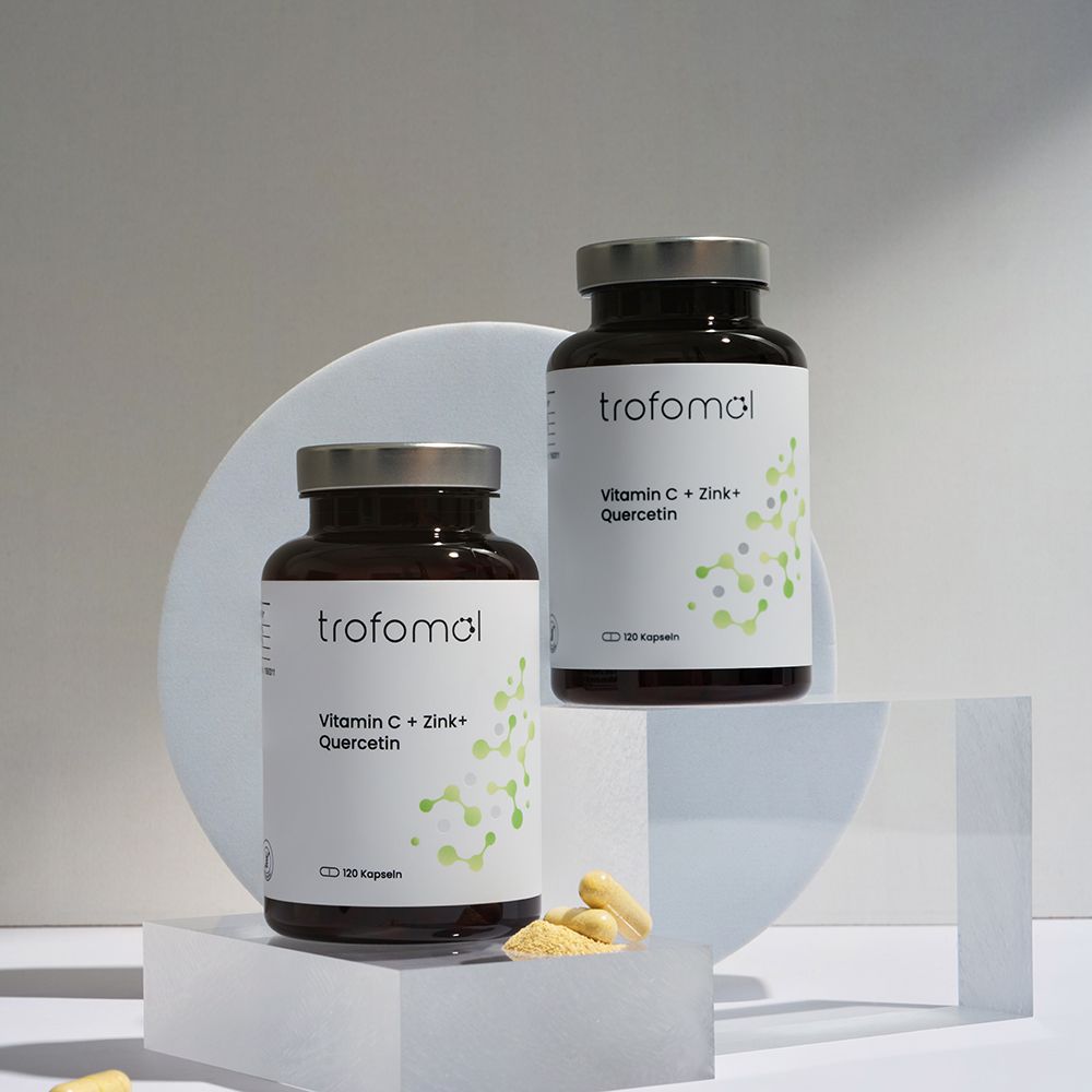Zwei braune Glasflaschen mit silbernen Deckeln und weißen Etiketten. Aufschrift: "trofomol", "Vitamin C + Zink + Quercetin". Kapseln liegen davor.