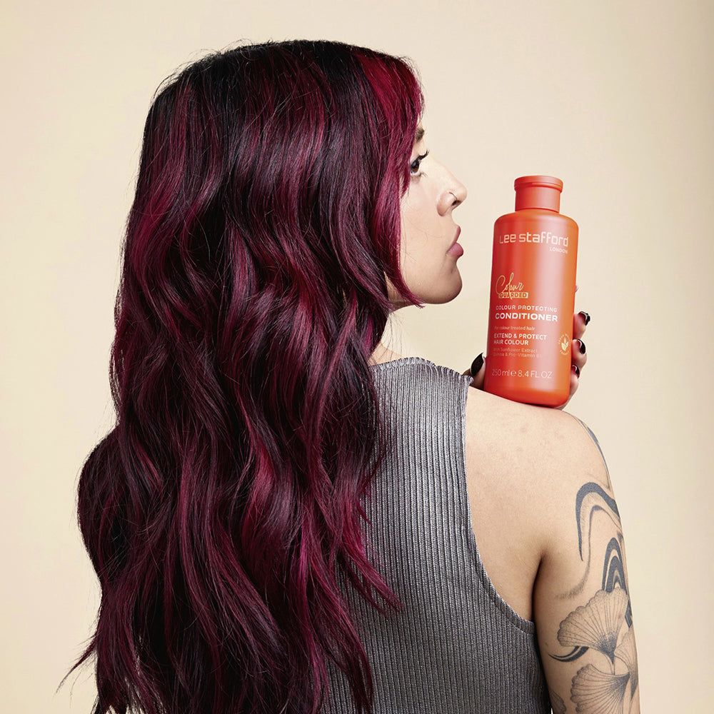 Eine Frau mit gefärbtem Haar hält eine orangefarbene Flasche Lee Stafford Colour Guarded Conditioner.