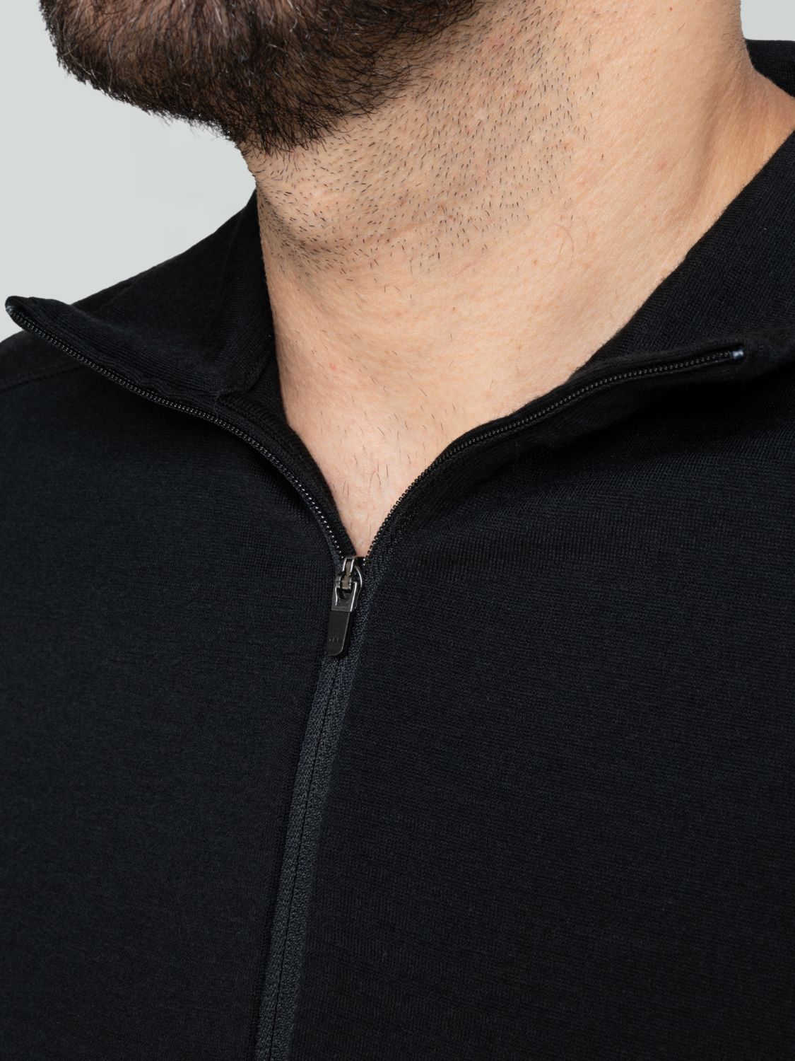 Nahaufnahme des Reißverschlusses und Kragens eines schwarzen Herren-Merino-Pullovers.