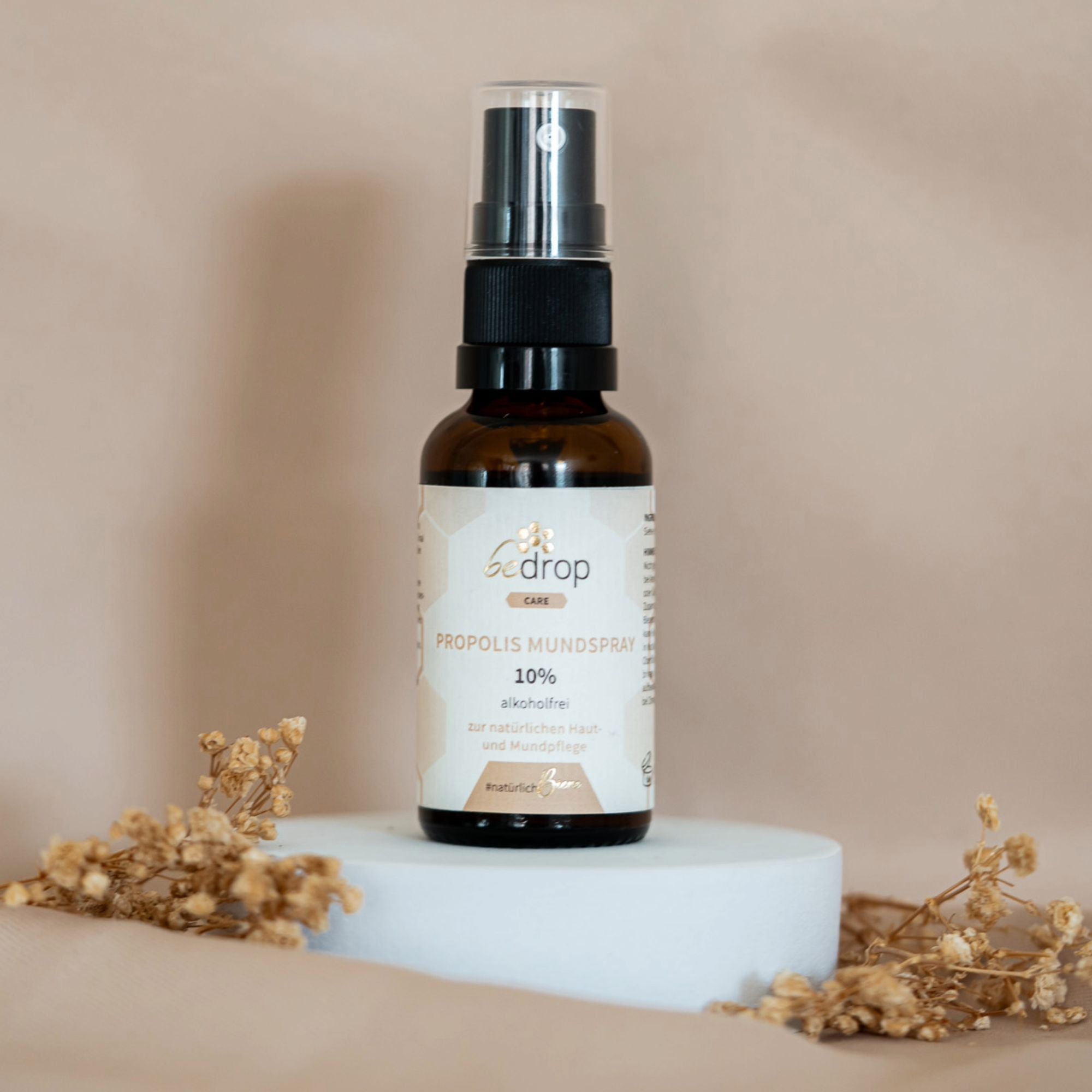 Braune Sprühflasche mit schwarzem Verschluss auf weißem Podest. Aufschrift: bedrop care, Propolis Mundspray 10% alkoholfrei.