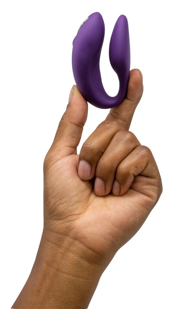Hand hält lila We-Vibe Chorus. Geschwungene Form. Produkt wird zwischen Fingern gehalten. Hautfarbe.