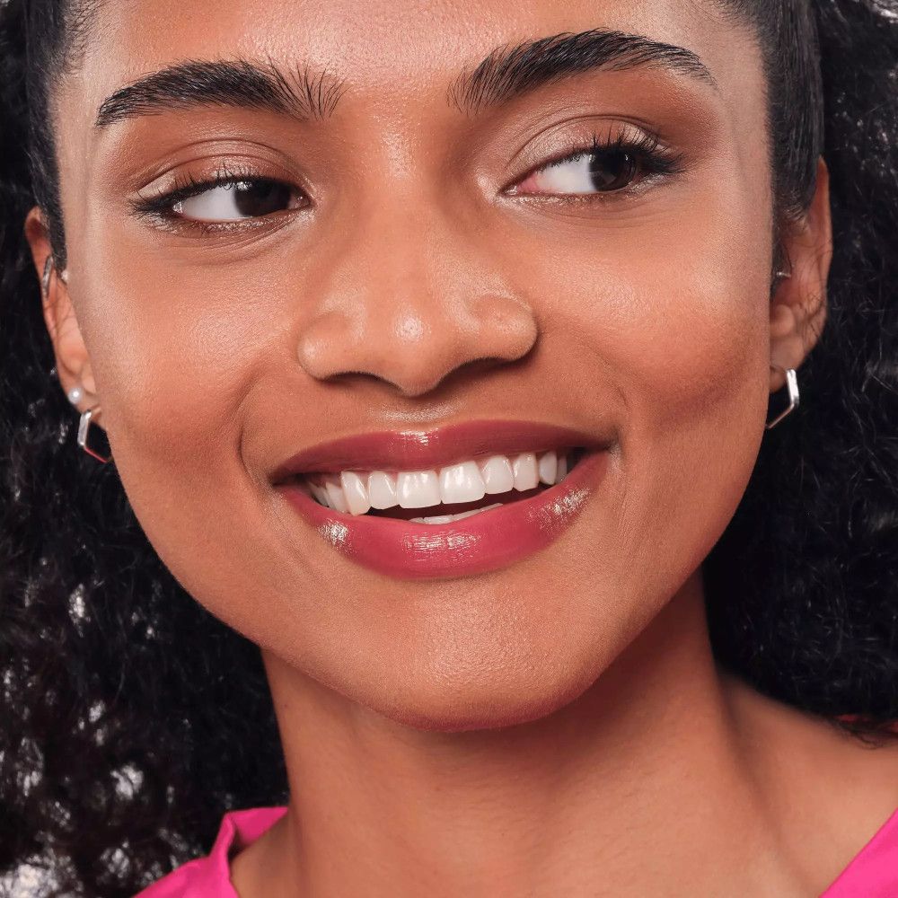 Porträt einer Frau mit Essence Hydra Kiss Lippen-Tint auf den Lippen. Sie lächelt, trägt Ohrringe.