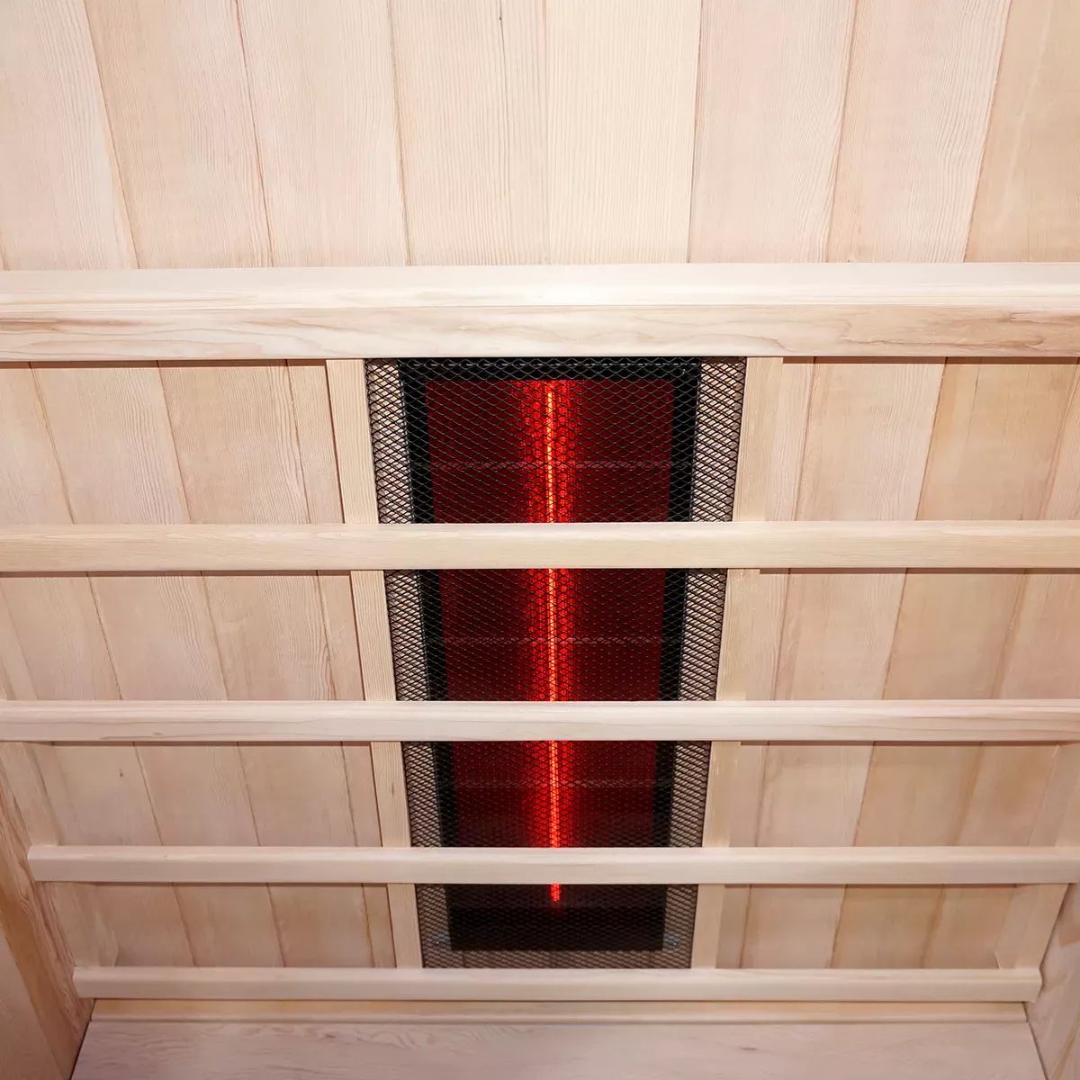 Blick in die Decke einer Infrarotsauna. Sichtbar sind Holzleisten und ein Infrarotstrahler mit Schutzgitter.