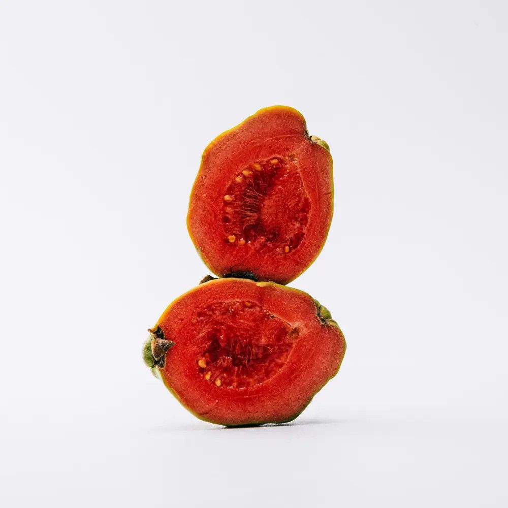 Zwei Hälften einer Guave, auf weißem Hintergrund. Rotes Fruchtfleisch mit kleinen Kernen. Grüne Schale.