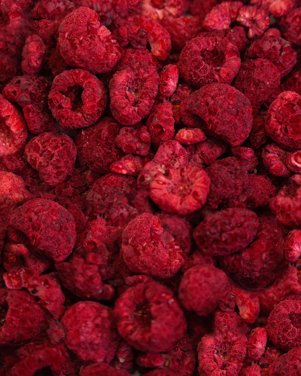 Nahaufnahme von gefriergetrockneten Himbeeren. Die roten Früchte sind unregelmäßig geformt und liegen dicht beieinander.