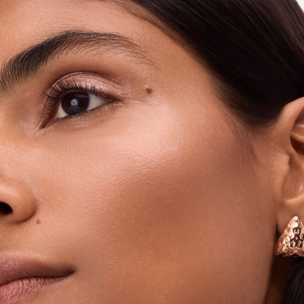 Nahaufnahme eines Gesichts mit aufgetragenem Highlighter. Fokus auf das Auge und die Wangenknochen.