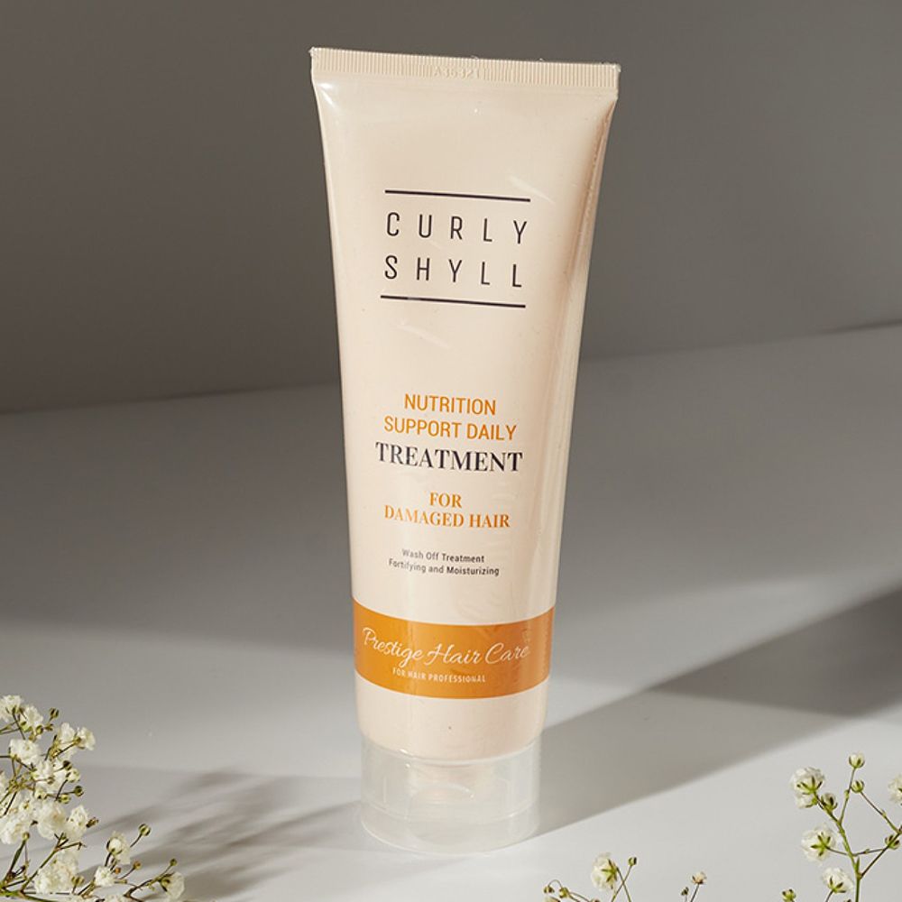 Beige Tube mit Produktnamen und Text. Auf weißem Untergrund. Blumen im Hintergrund.