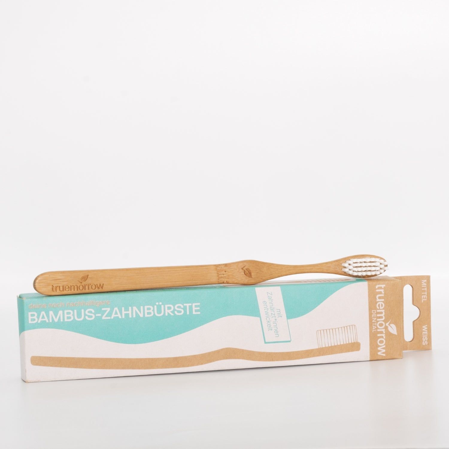 Zahnbürste aus Bambus mit weißem Borstenkopf und Verpackung. Auf der Verpackung steht "Bambus-Zahnbürste" und der Markenname "truemorrow".