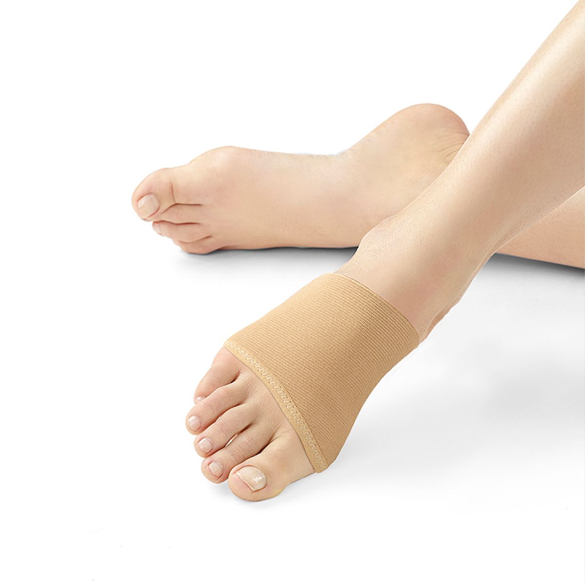 Beige Hallux Valgus Bandage am Fuß. Elastisches Material, bedeckt den Vorfuß. Der Fuß ist auf weißem Hintergrund.