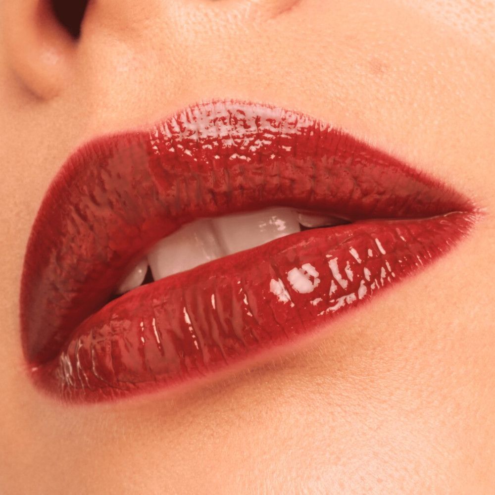 Nahaufnahme von Lippen mit glänzendem, dunkelrotem Lippenstift. Zähne sichtbar.