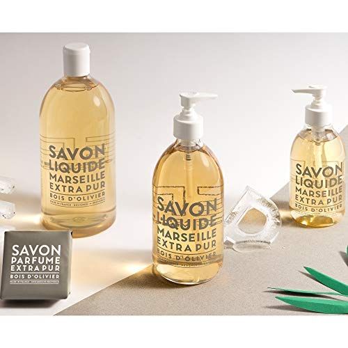 Drei Flaschen Flüssigseife und eine Seife. Aufschrift: Savon Liquide Marseille Extra Pur Bois d'Olivier.