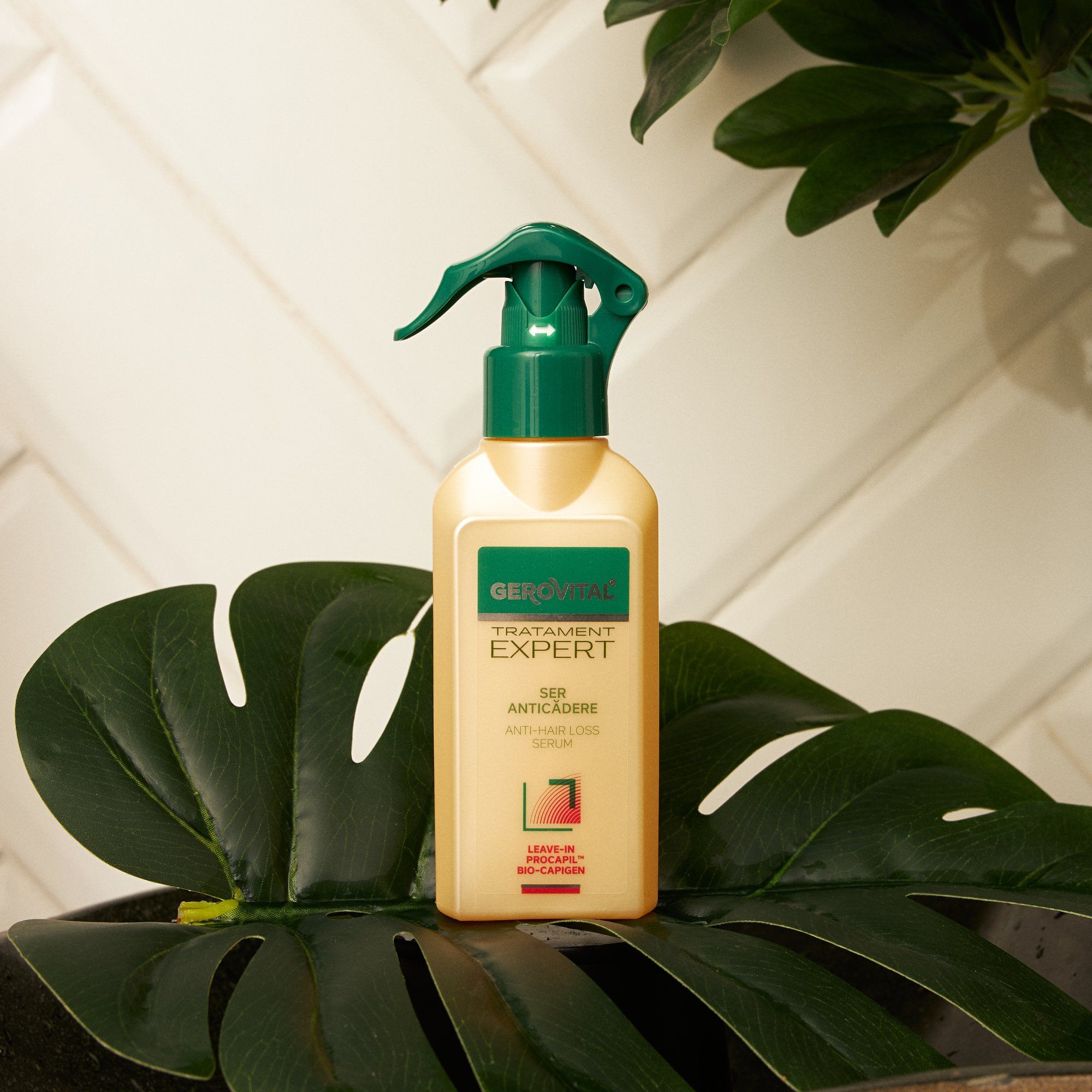 Beige Flasche mit grünem Sprühkopf. Aufschrift: Gerovital Tratament Expert, Ser Anticadere, Anti-Haarausfall Serum. Auf Blatt platziert.