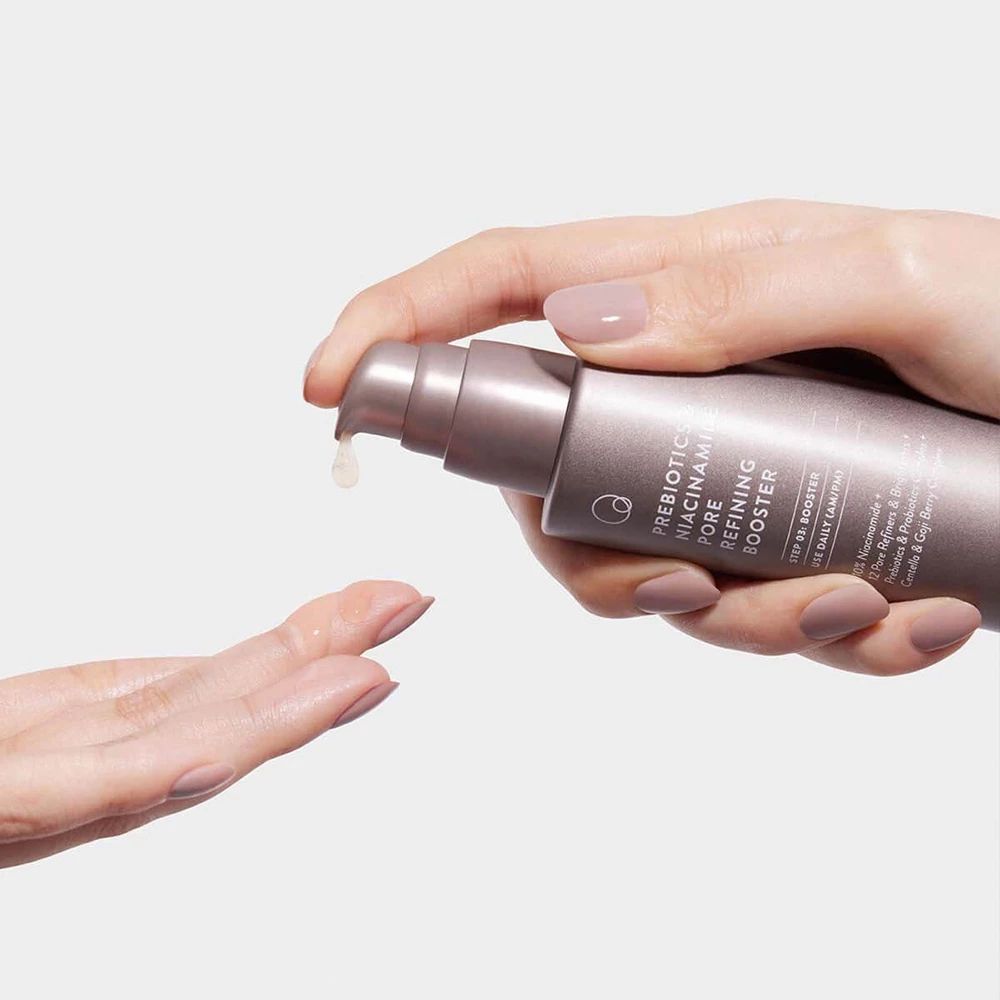 Hand hält Flasche und gibt Flüssigkeit ab. Beschriftung: Prebiotics & Niacinamide Pore Refining Booster. Flüssigkeit tropft auf Hand.