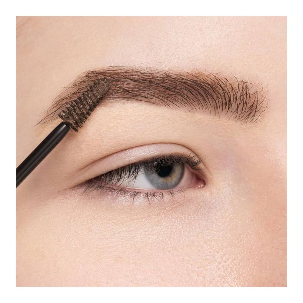 Auge mit Augenbraue, die mit einem Bürstchen bearbeitet wird. Bürste und Augenbraue sind braun.