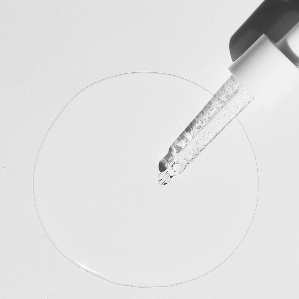 Pipette mit Flüssigkeit. Flüssigkeit tropft auf eine kreisförmige Fläche. Weißer Hintergrund.