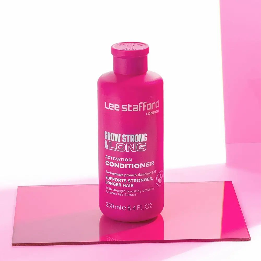 Rosa Flasche 'Grow Strong & Long Conditioner' auf einer rosa Glasplatte. Produktname und Marke sind sichtbar.