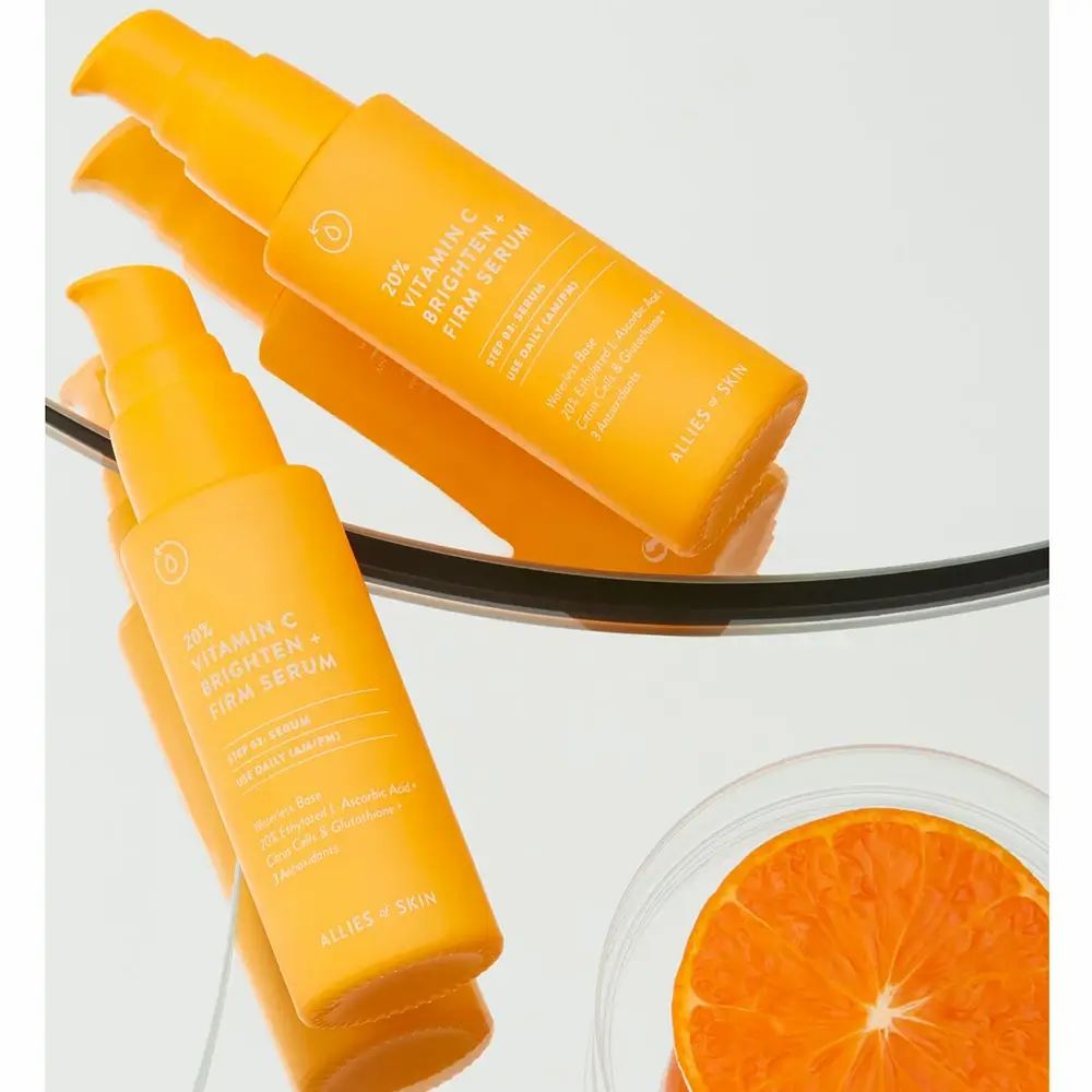 Zwei gelbe Flaschen mit Serum. Text: 20% Vitamin C Brighten + Firm Serum. Marke: ALLIES OF SKIN. Spiegelung.