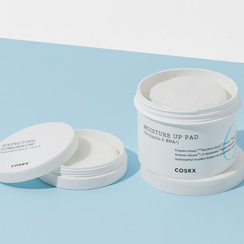 Geöffnete weiße Dose mit Pads. Deckel daneben. Aufschrift 'MOISTURE UP PAD'. Marke: COSRX.