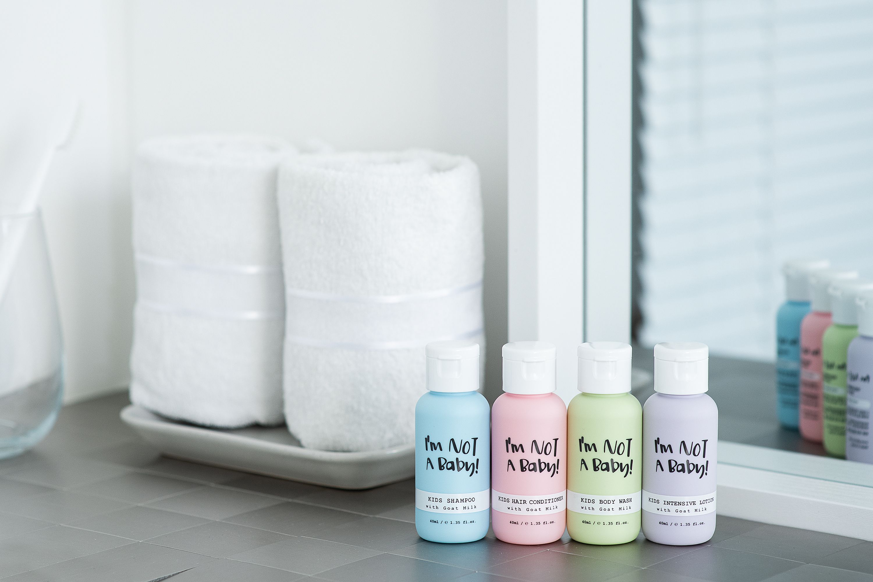 Vier kleine bunte Flaschen mit "I'm NOT A Baby!" Aufschrift: Shampoo, Conditioner, Body Wash, Body Lotion.