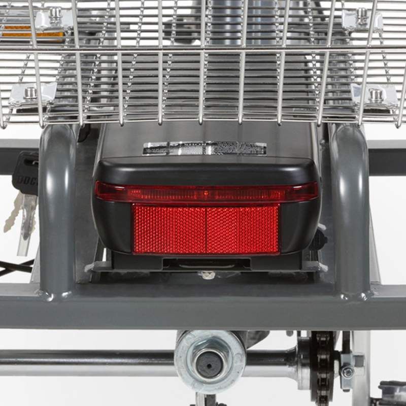 Nahaufnahme des Rücklichts des Elektro-Dreirads »Mobil«. Rotes Licht, schwarzes Gehäuse, silberne Halterung, Korb.
