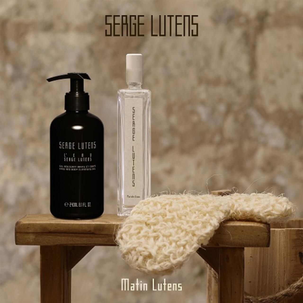 Eine Flasche mit Pumpe und eine Flasche auf einer Holzbank. Text: Serge Lutens. Bürste und Holzfass.