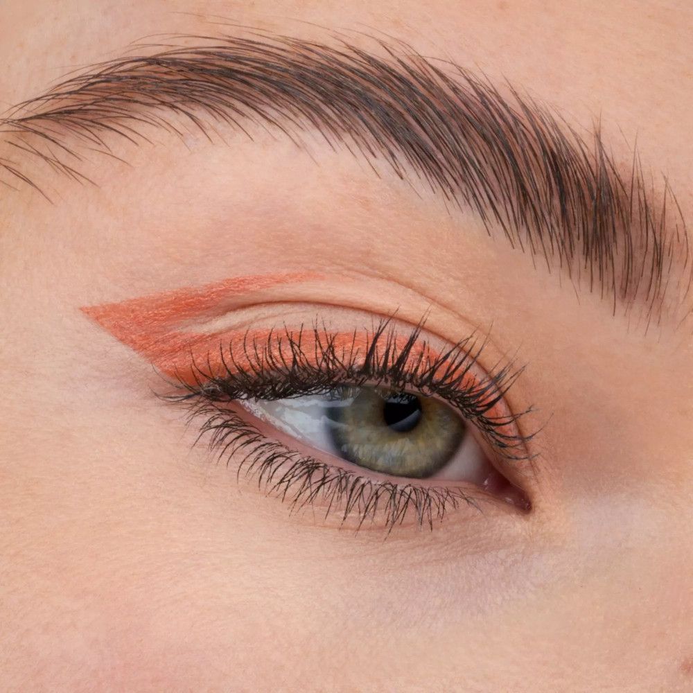 Auge mit orangefarbenem Eyeliner-Strich. Wimpern und Augenbraue sichtbar.