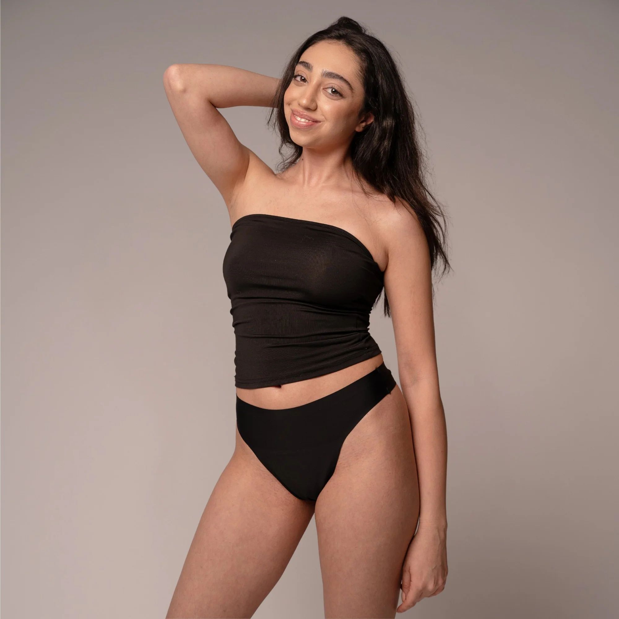 Frau in schwarzem Top und Slip, lächelnd. Sie stützt ihren Arm.