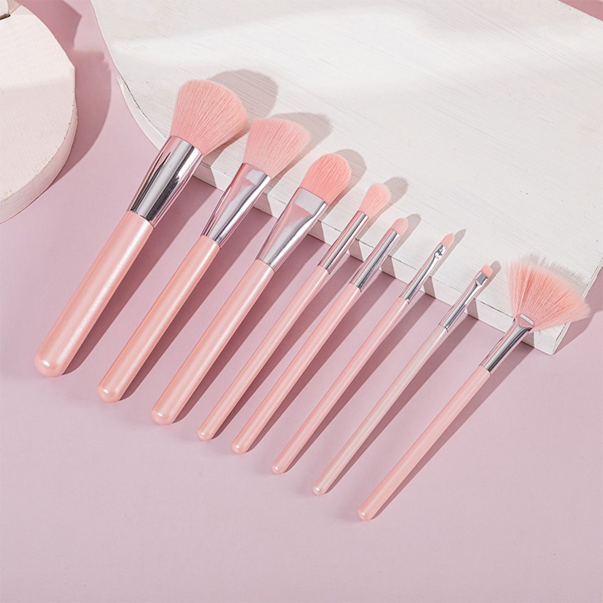Ein Set aus sieben rosa Make-up-Pinseln mit silbernen Akzenten, auf einem rosa Untergrund.