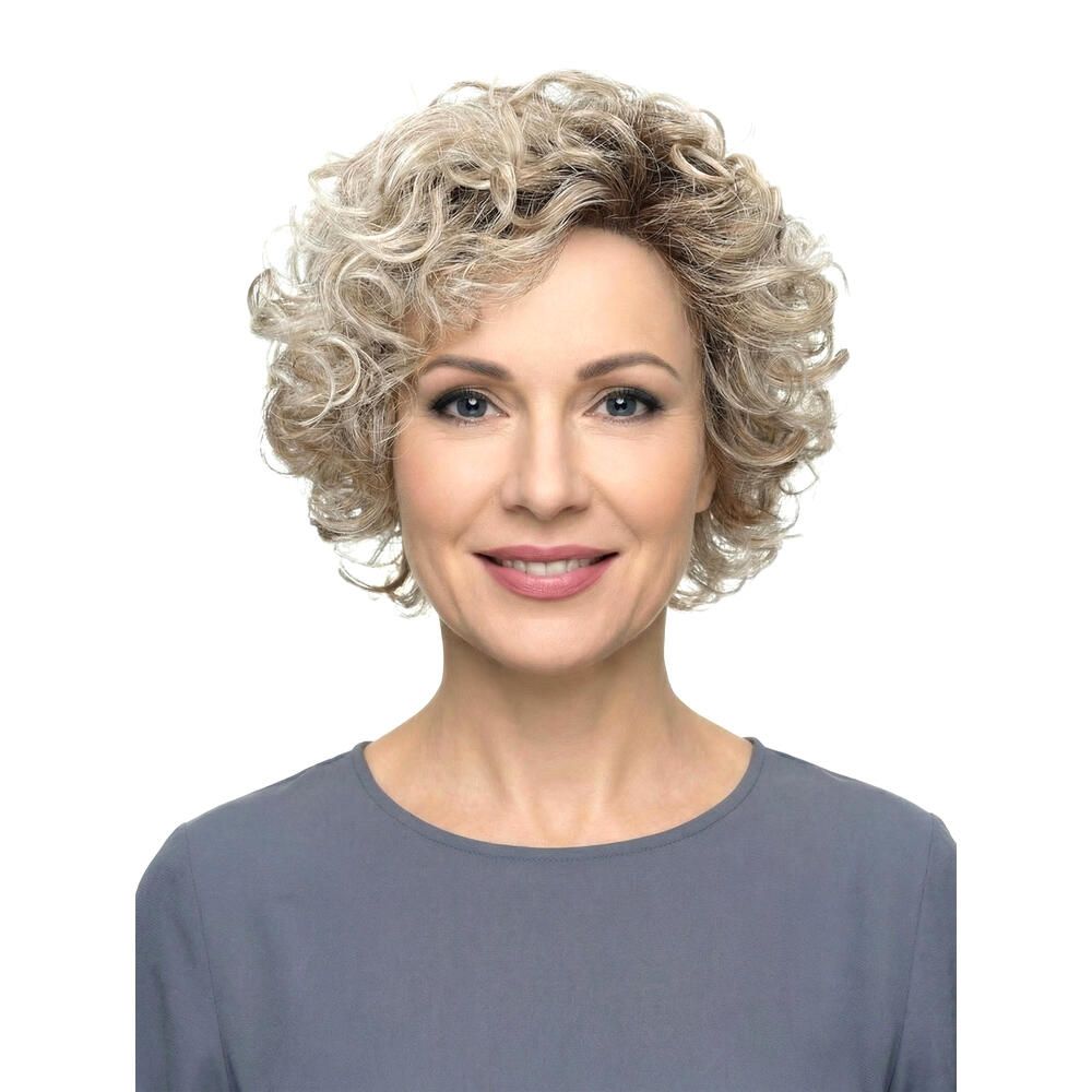 Frau mit Perücke, blond gelockt, Frontansicht. Graues Oberteil. Natürlicher Teint, lächelt.