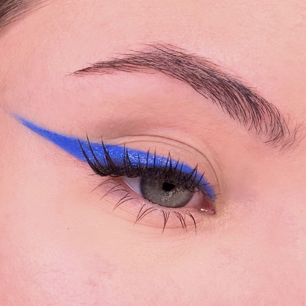 Auge mit blauem Eyeliner. Blauer Lidstrich über dem oberen Wimpernkranz. Wimpern und Augenbraue sichtbar.
