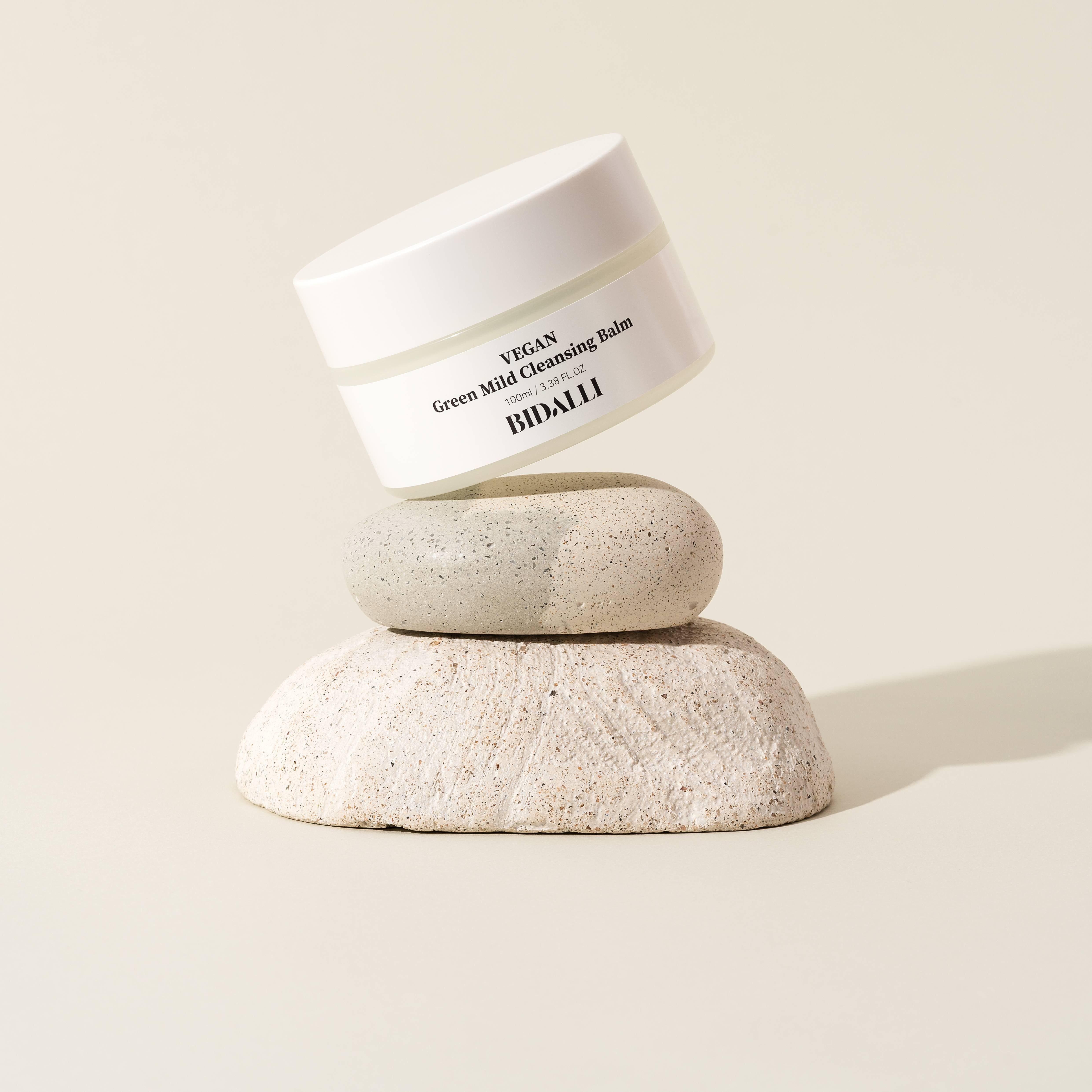 Weißer Tiegel auf Steinen. Auf dem Etikett steht: VEGAN Green Mild Cleansing Balm. Darunter: BIDALLI.