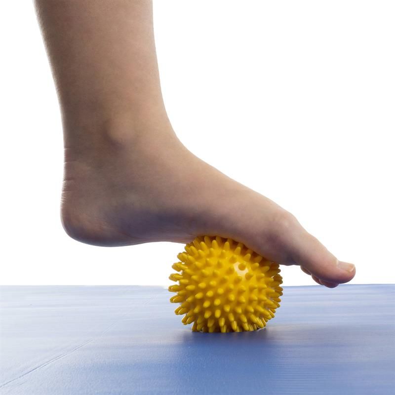 Gelbe Massagekugel mit Noppen unter einem Fuß. Der Fuß liegt auf der Kugel, die auf einer blauen Oberfläche liegt.