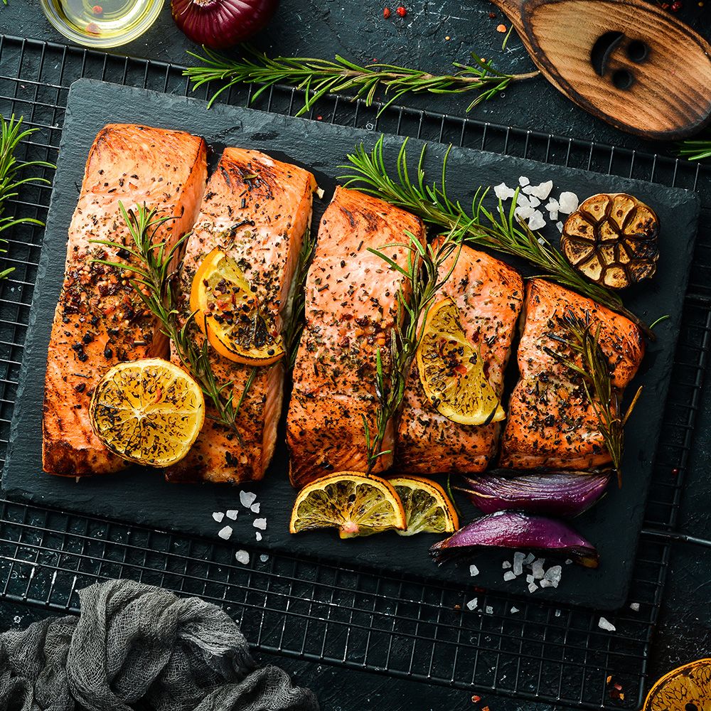 Gebratener Lachs auf schwarzem Schieferbrett. Mit Rosmarin, Zitronenscheiben und Gewürzen. Draufsicht.
