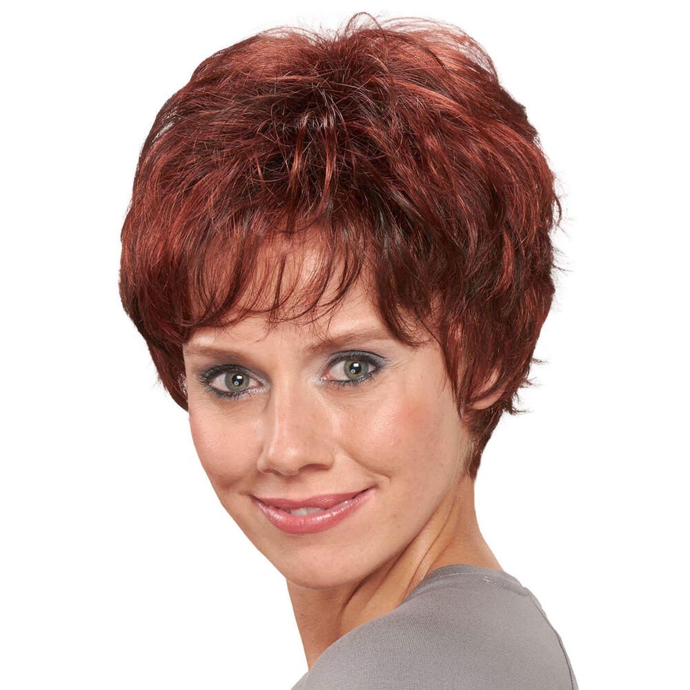 Kurzhaarperücke in Rotbraun. Frau lächelt. Blick nach vorn. Lockige Struktur. Pony. Graues Oberteil.