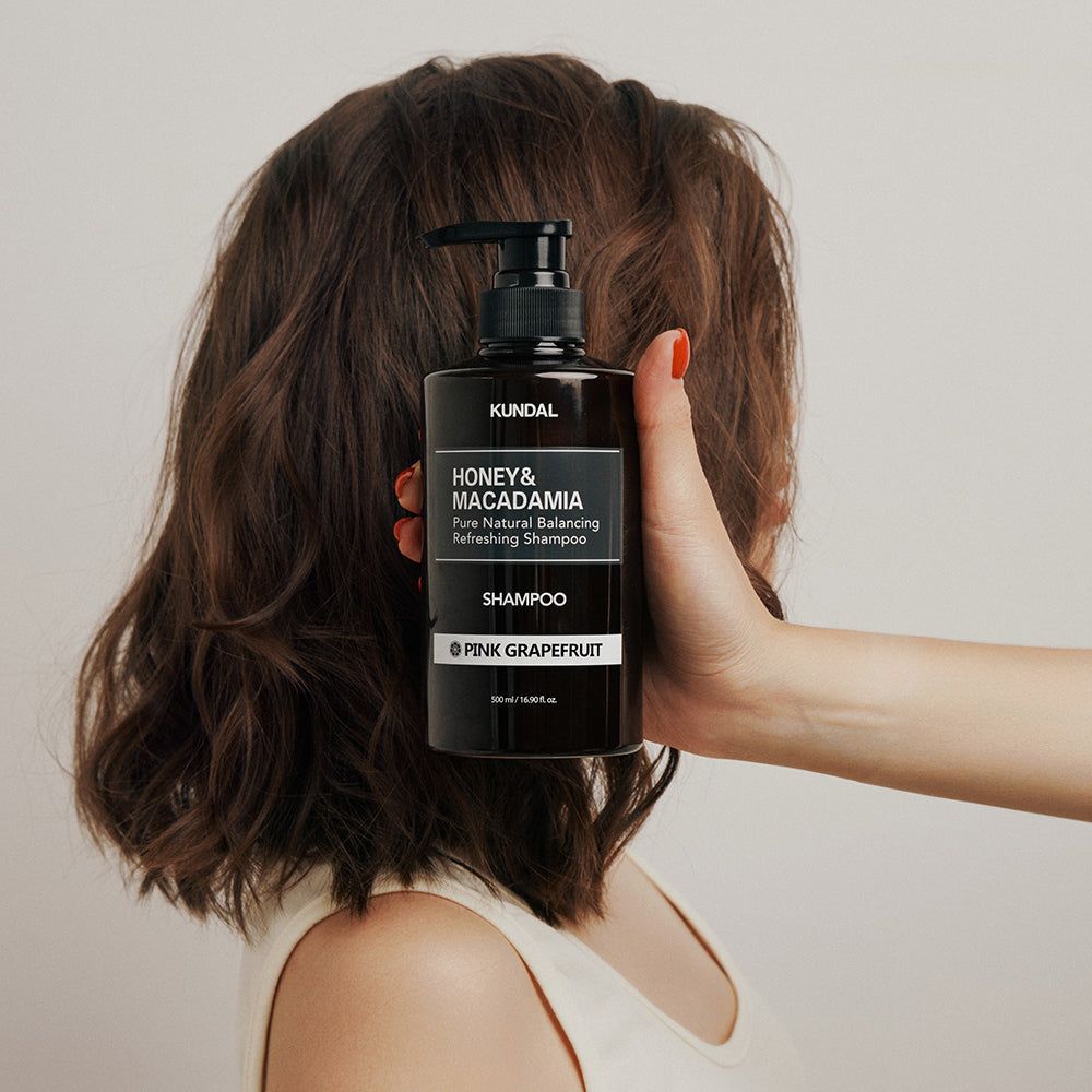 Eine Hand hält eine braune Shampoo-Flasche vor dem Haar einer Person.