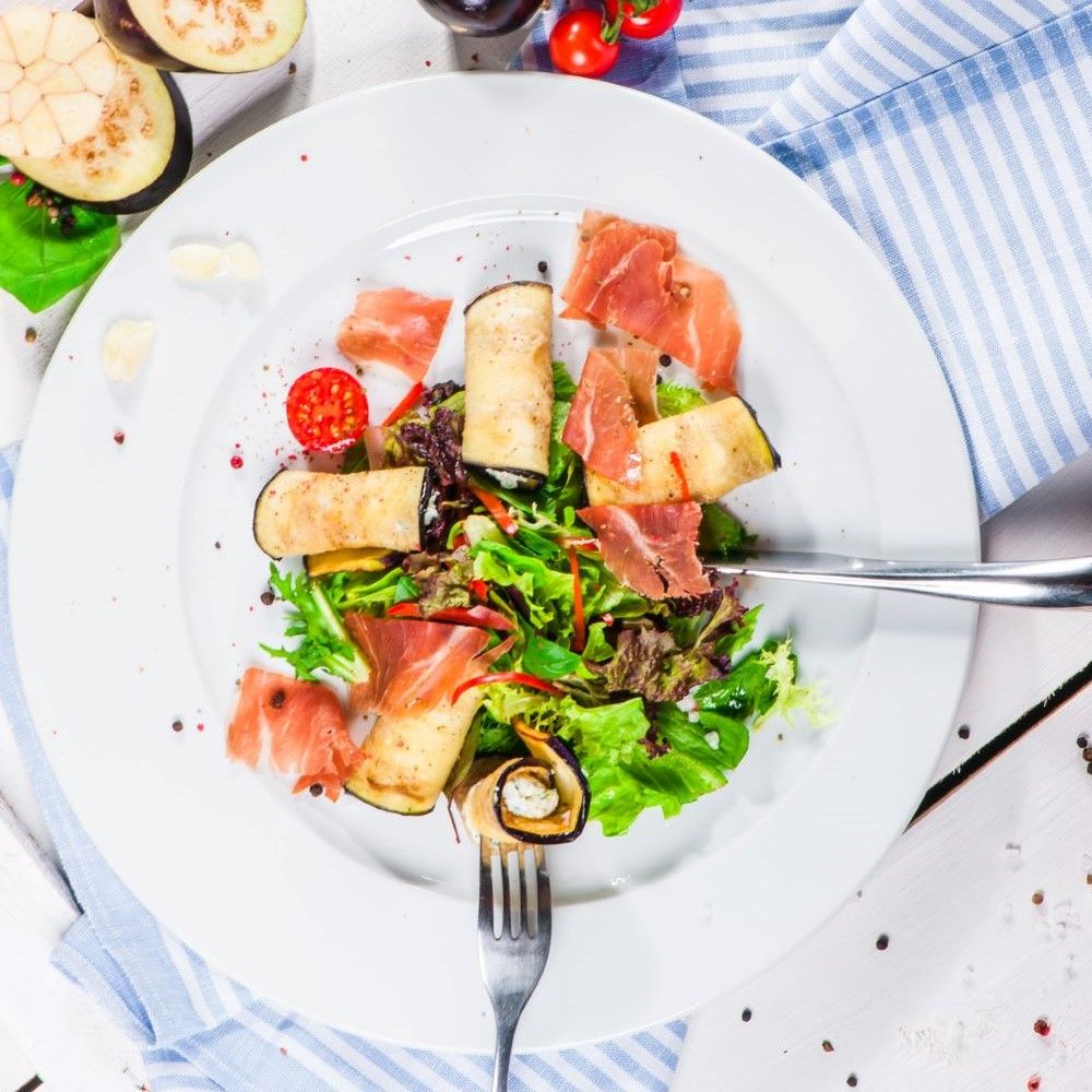 Teller mit Salat, Auberginenröllchen, Schinken und Tomaten. Gabel im Bild.