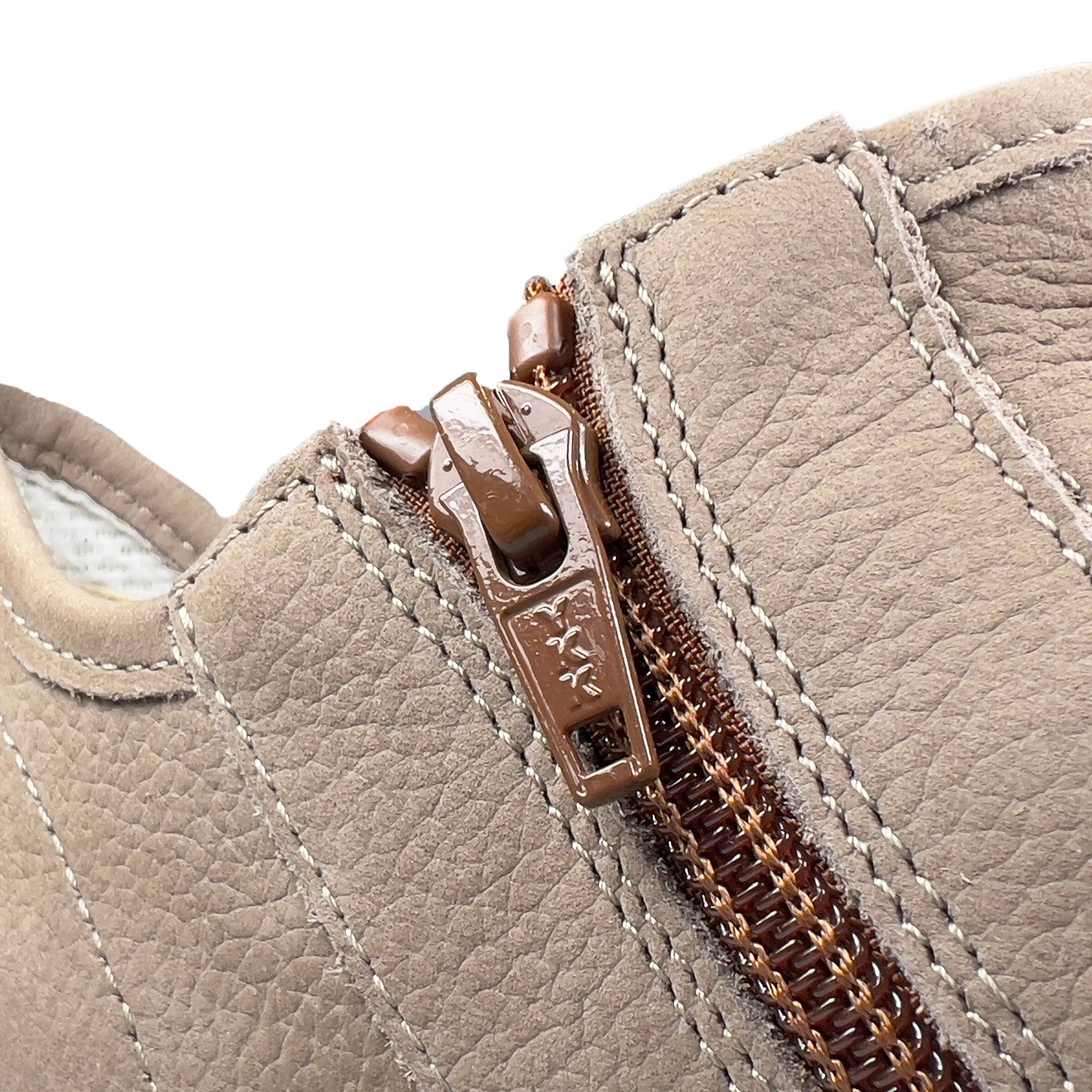 Nahaufnahme eines Schuhs mit braunem Reißverschluss. Beige Lederstruktur, sichtbare Nähte.