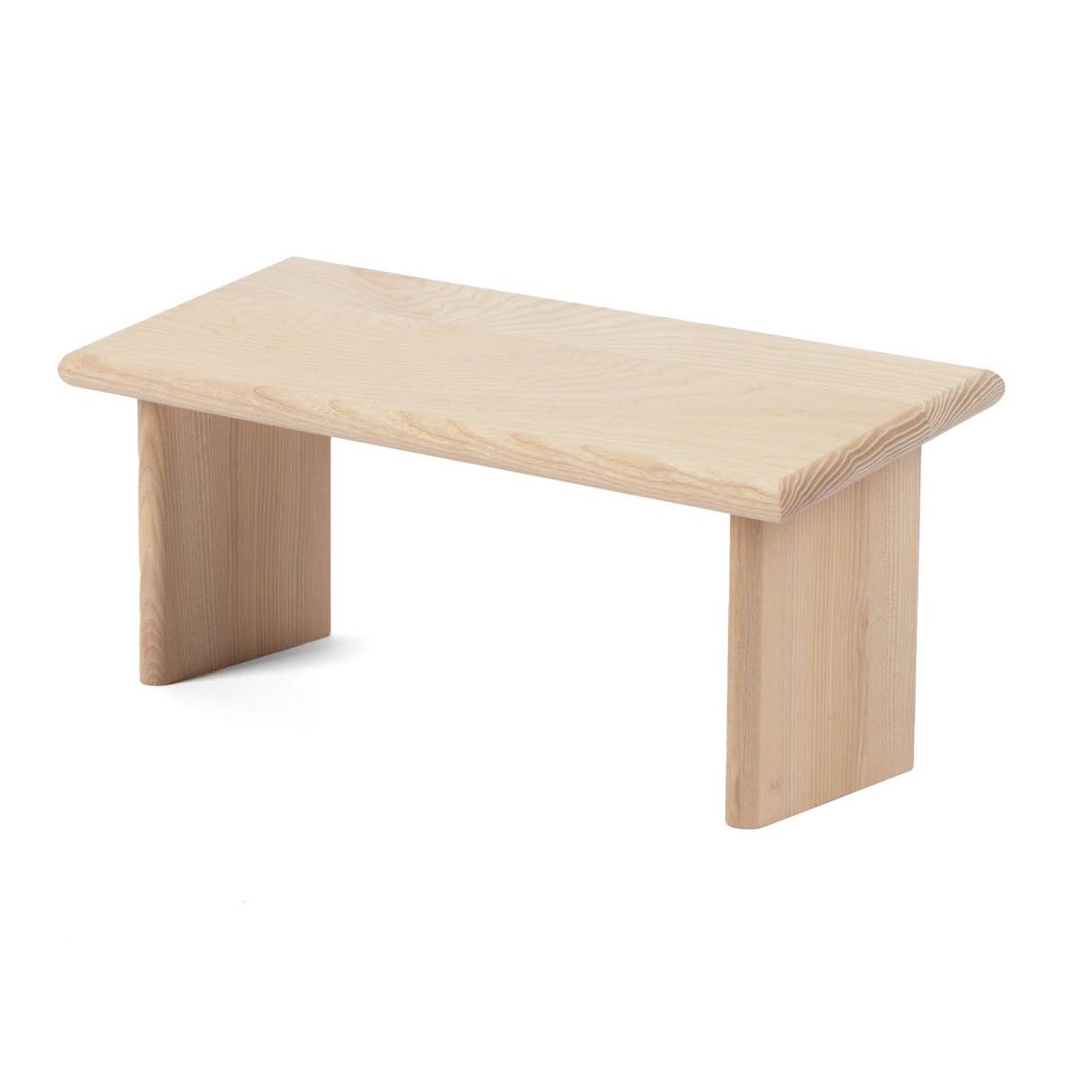 Hocker aus hellem Holz mit rechteckiger Sitzfläche und zwei Beinen. Abgerundete Kanten.