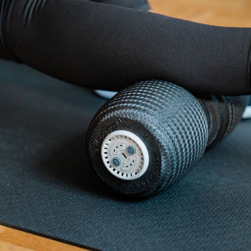 Nahaufnahme einer schwarzen Faszienrolle. Eine Person liegt mit dem Bein auf der Rolle. Die Rolle hat eine strukturierte Oberfläche.