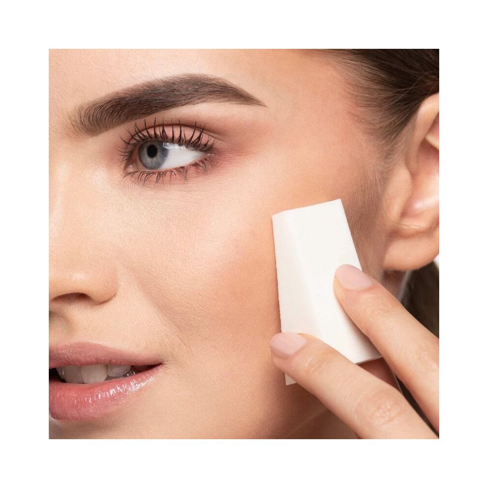 Eine Frau verwendet einen Make-up-Schwamm in Dreiecksform auf ihrer Wange.