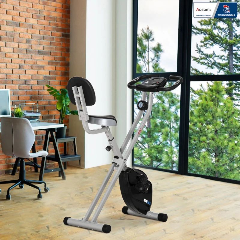 Heimtrainer in einem Raum. Sichtbar sind Fenster, Schreibtisch, Stuhl und Ziegelwand.